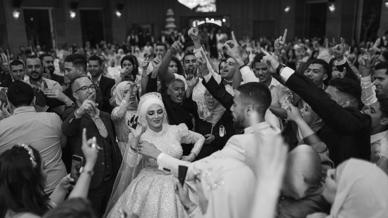 A bride dancing in a crowd of guests, some filming on their phones, in black and white