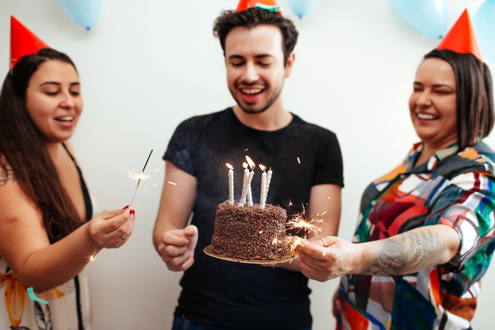 Friends celebrating a birthday with a candle-lit cake and party hats