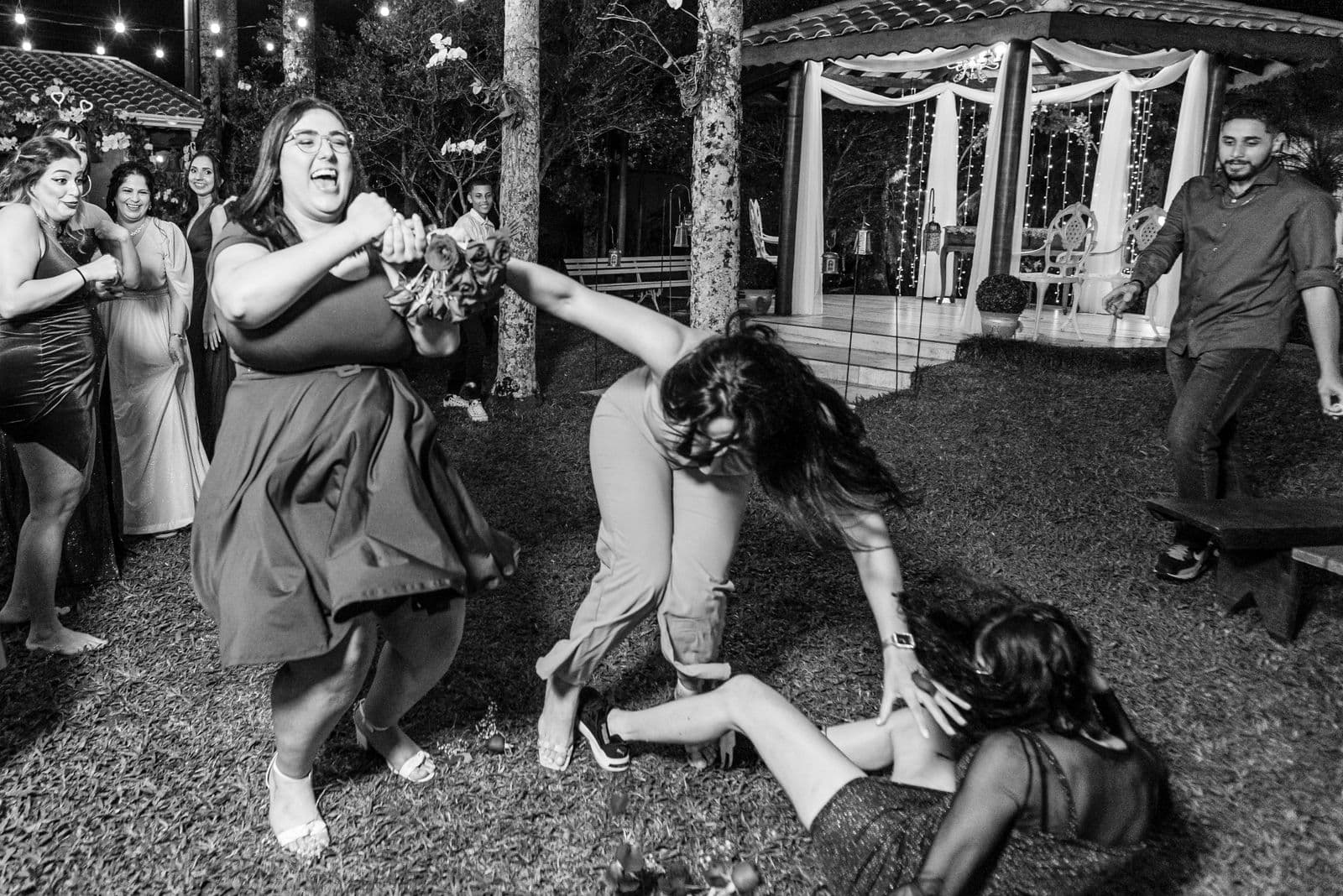 A candid black and white moment of guests catching the bouquet at a wedding
