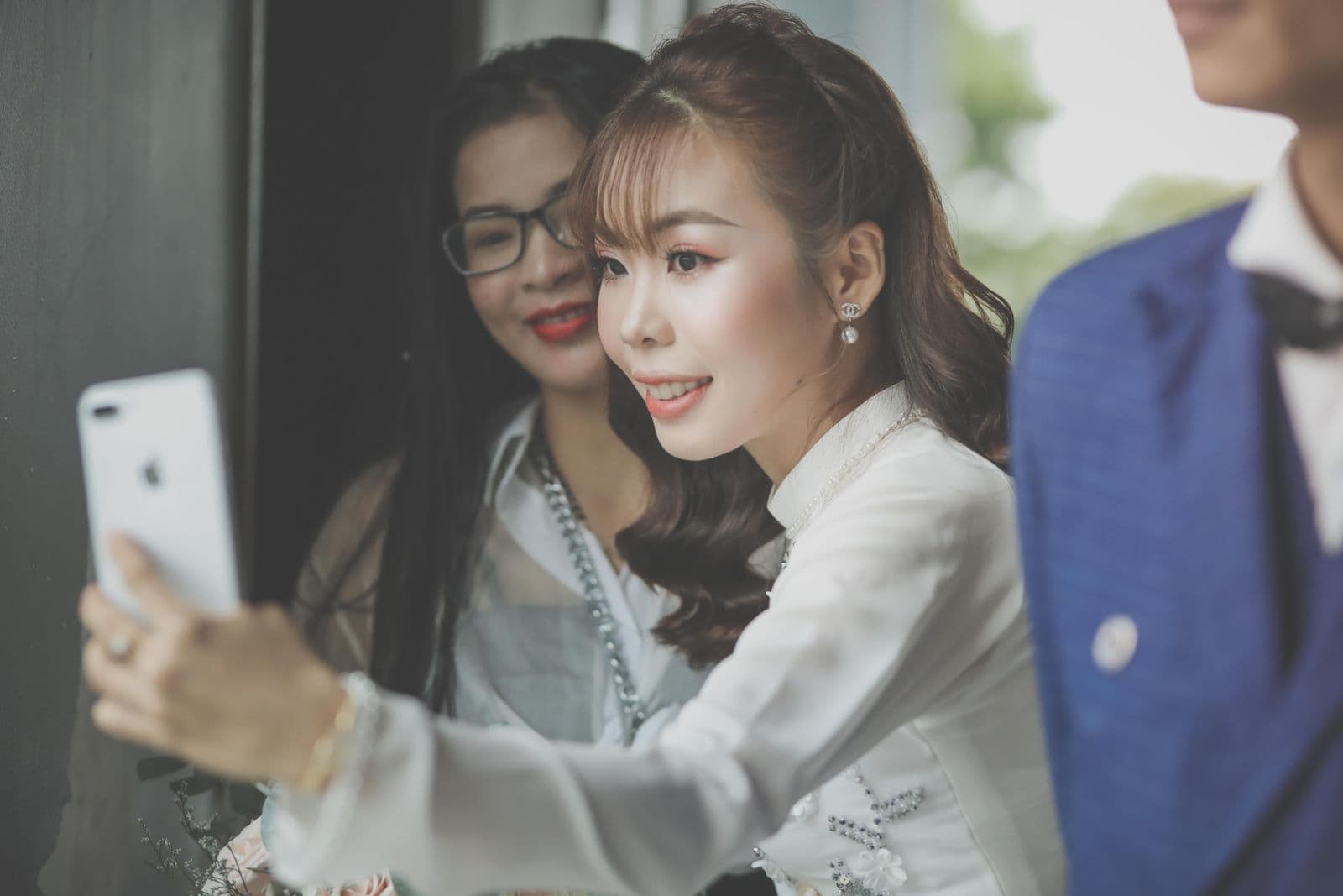 A bride taking a selfie with a guest on a phone at her wedding