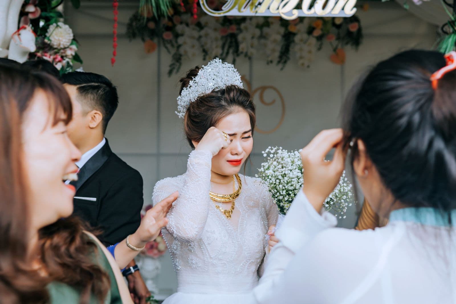 A bride wiping away a happy tear surrounded by guests at her wedding