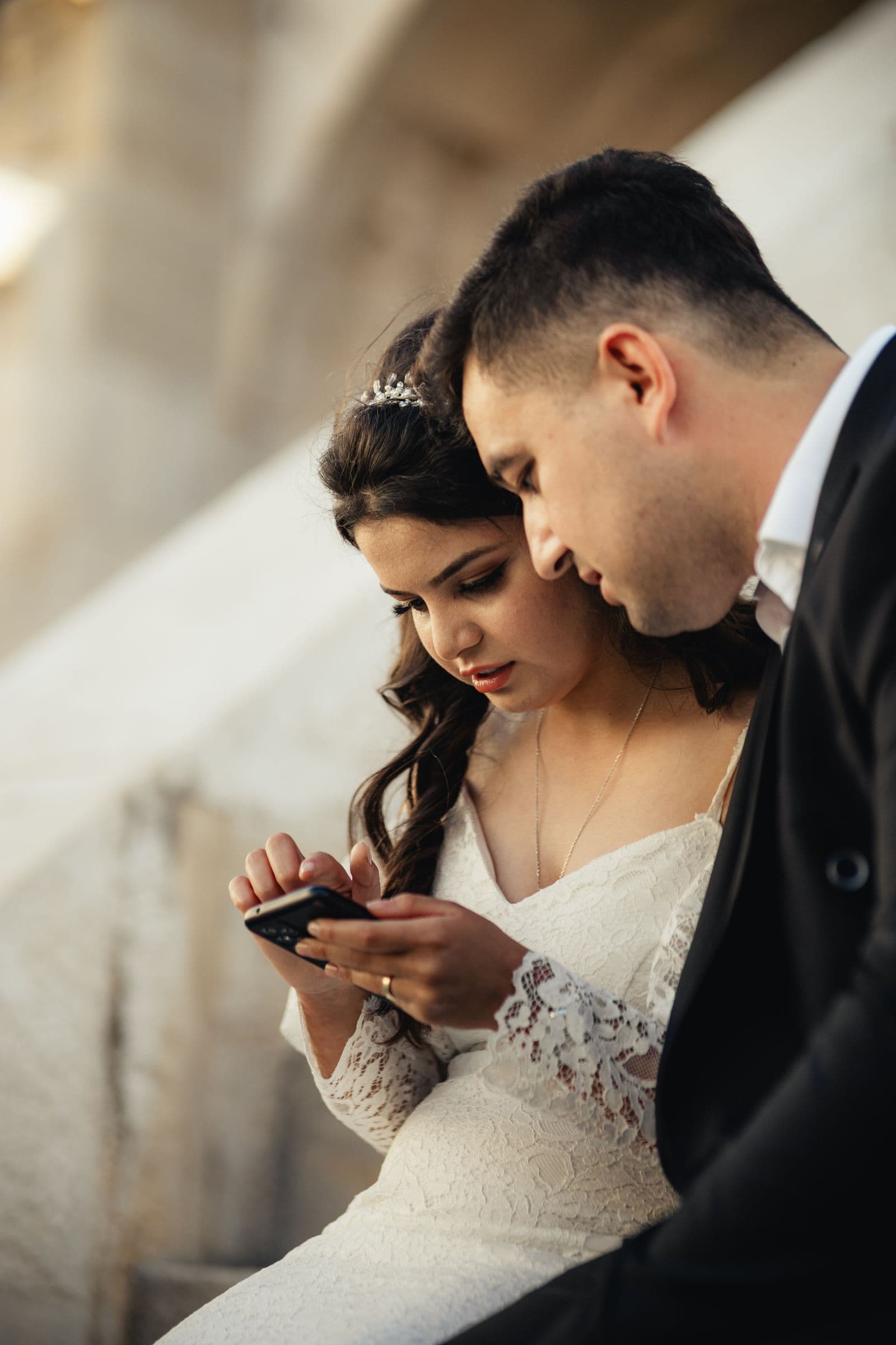 A bride and groom looking at a phone together on their wedding day