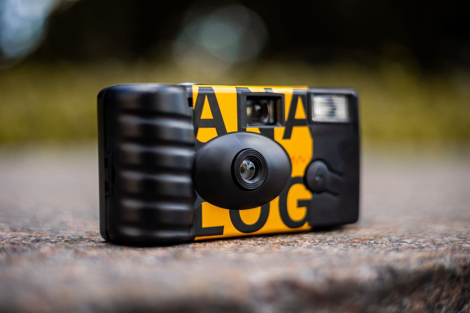 A single-use analog disposable camera resting on a stone surface