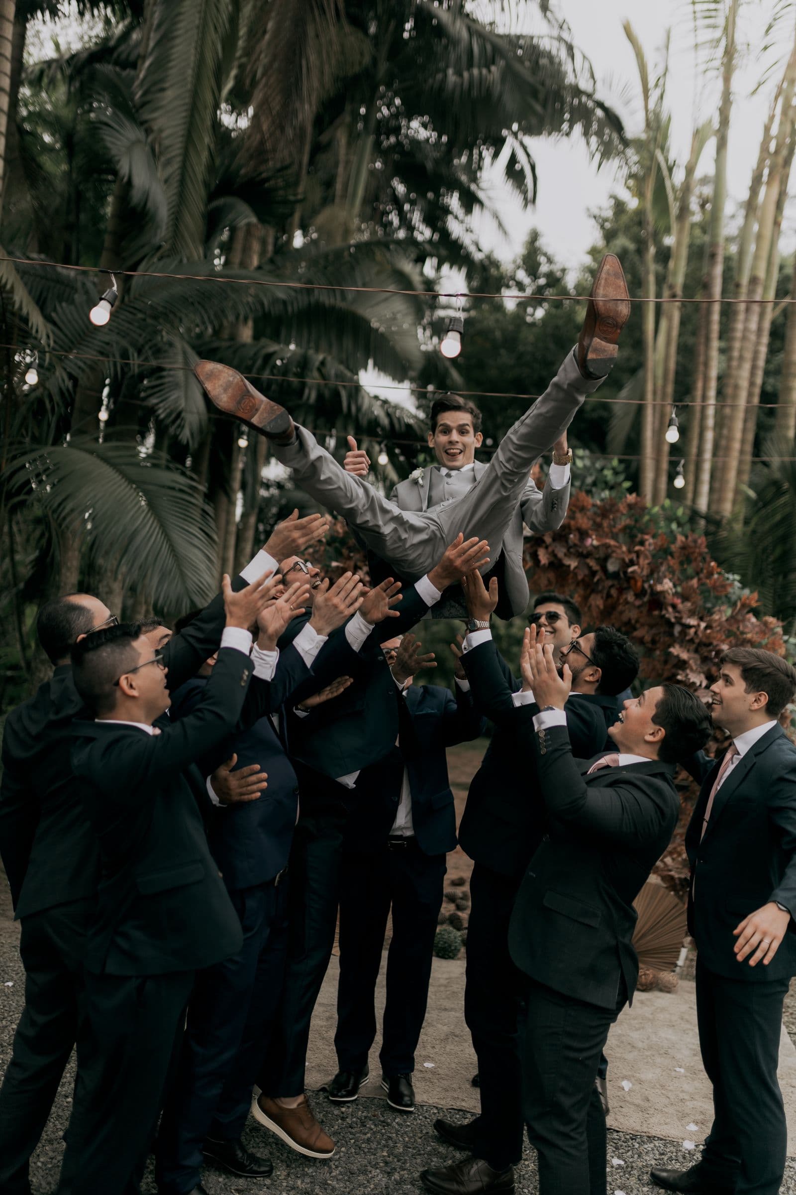 Groomsmen tossing the groom into the air at an outdoor wedding