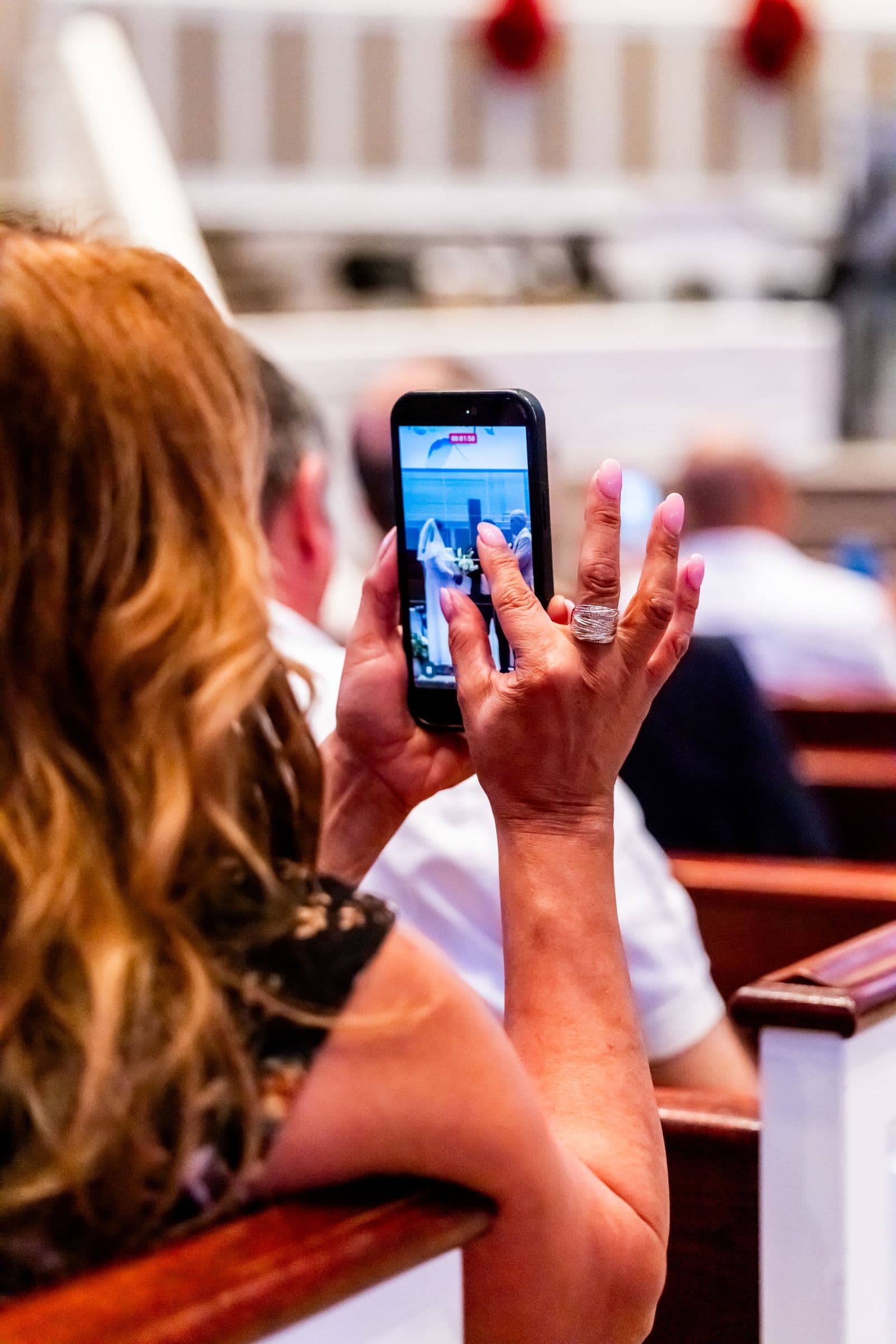 A wedding guest recording the ceremony on a phone from a pew