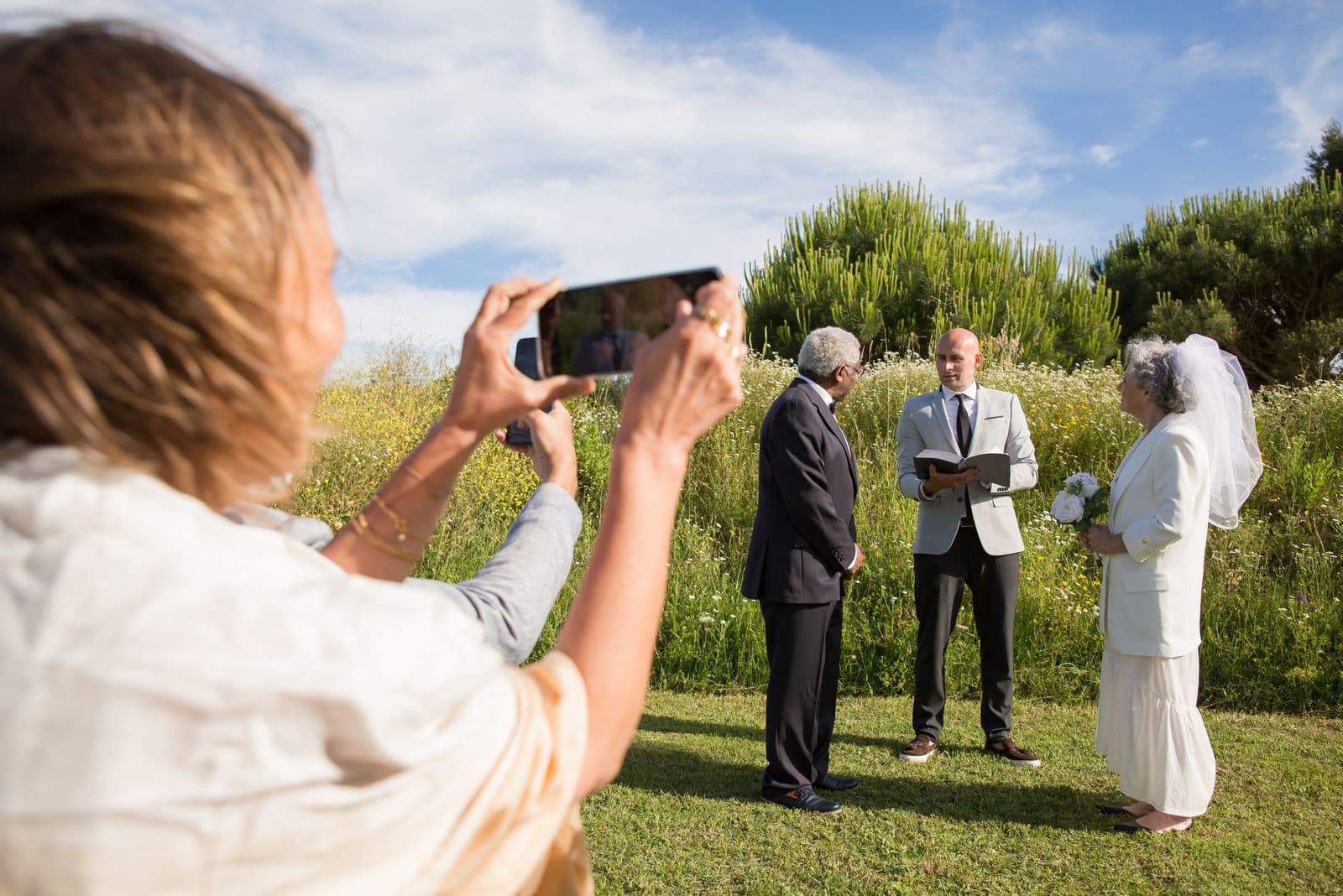 A wedding guest photographing an outdoor ceremony on her phone