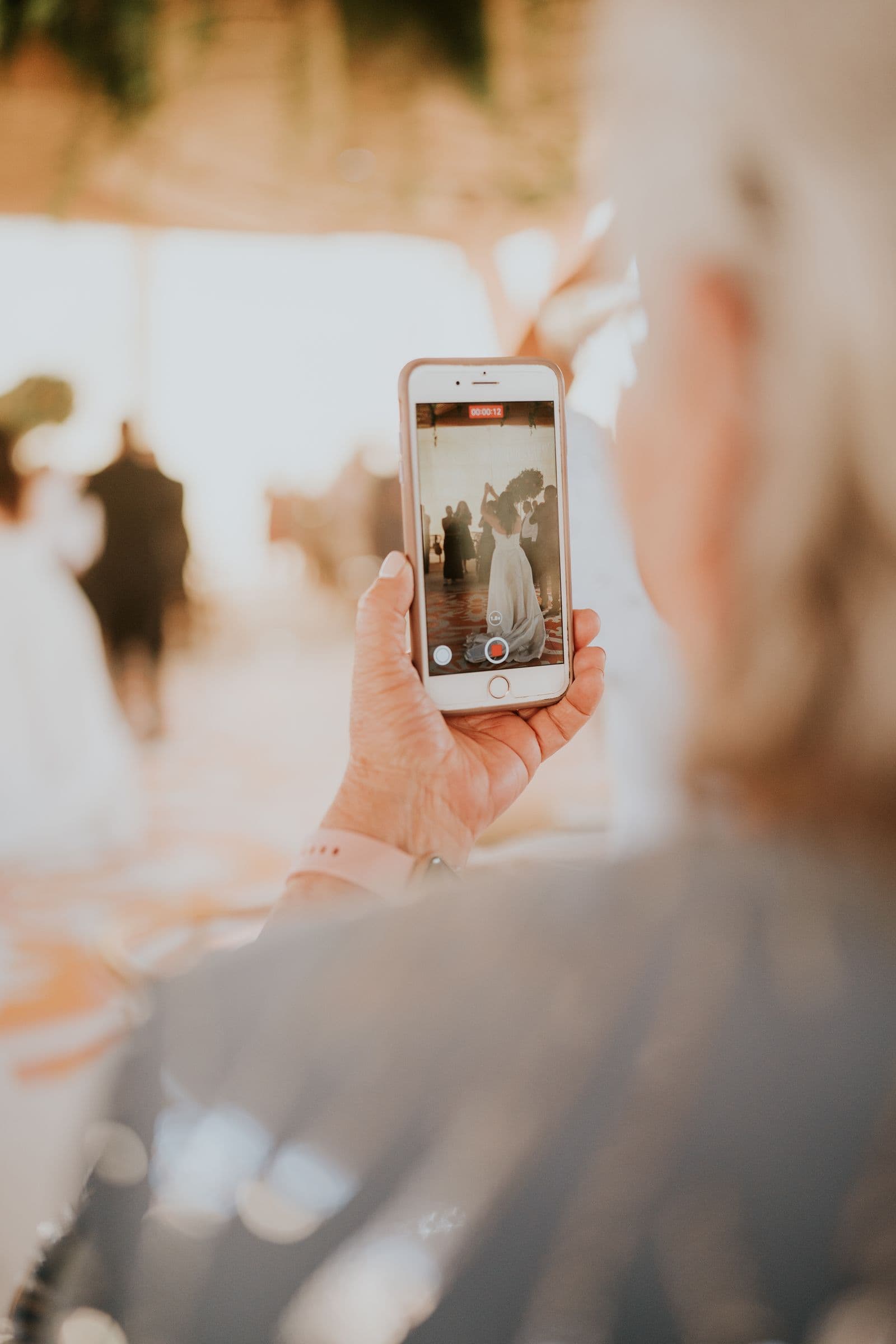 An older wedding guest recording the bride on a phone