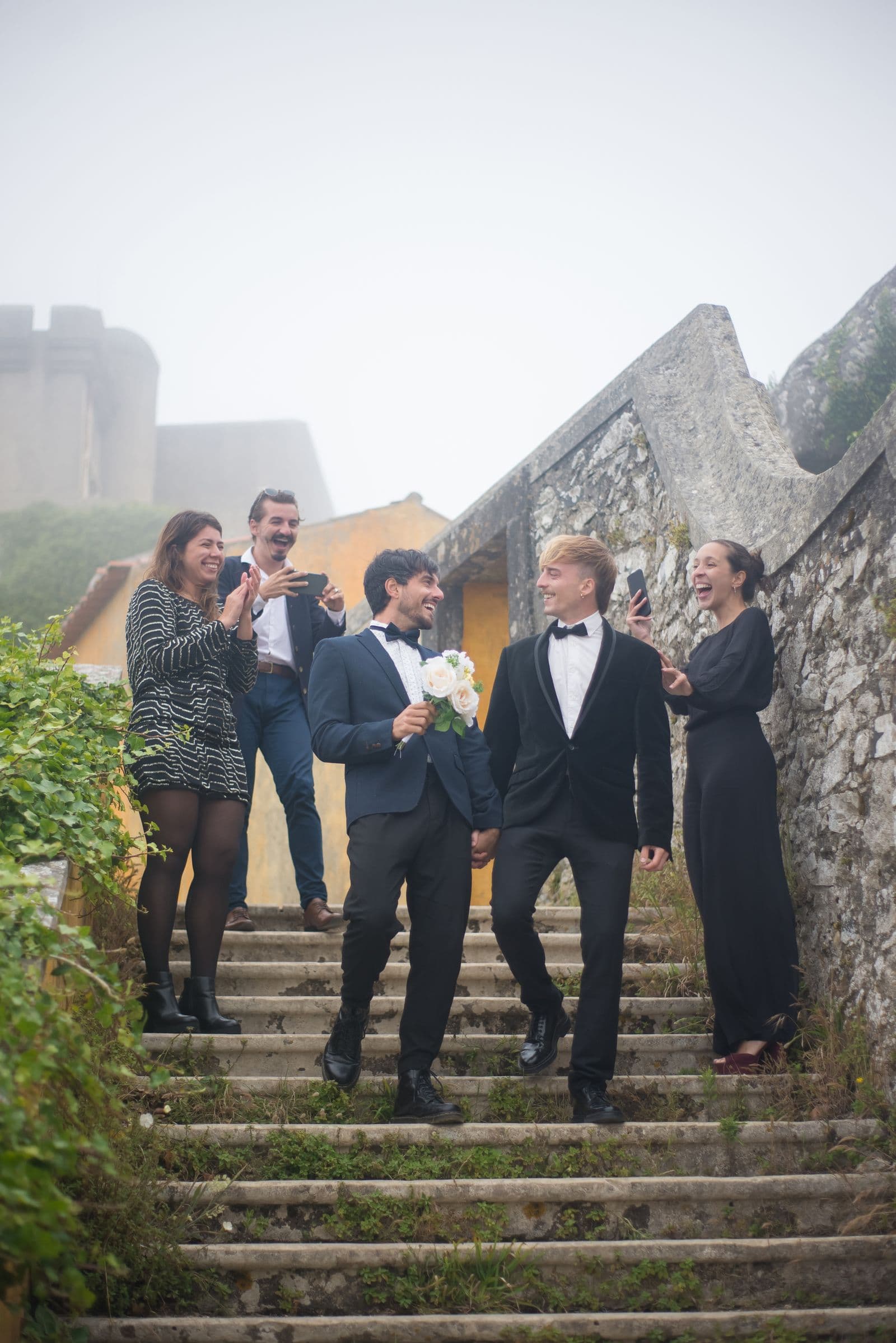 Wedding guests photographing the newlyweds on their phones as they walk down stone steps