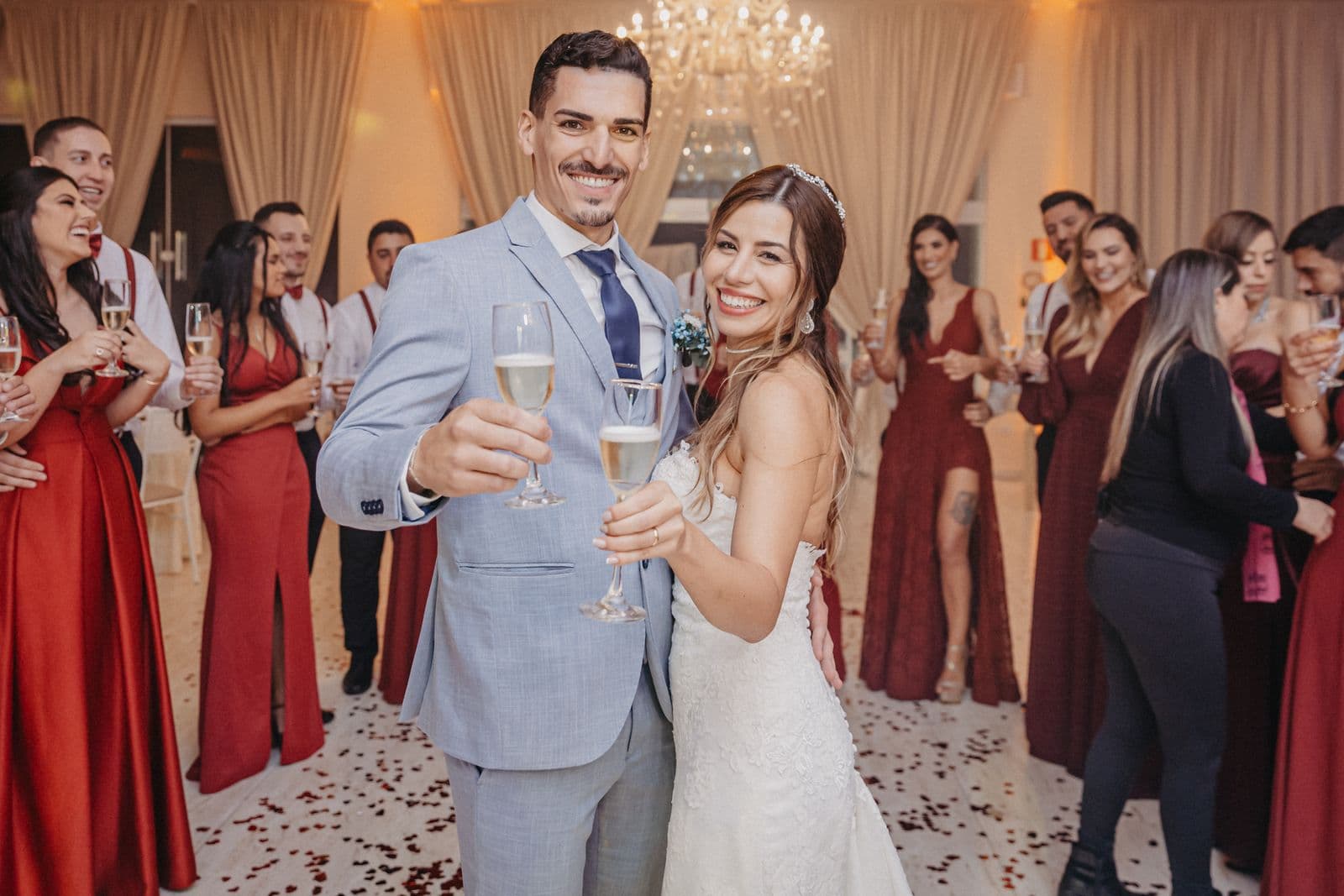 A smiling bride and groom toasting champagne with their wedding party gathered behind them