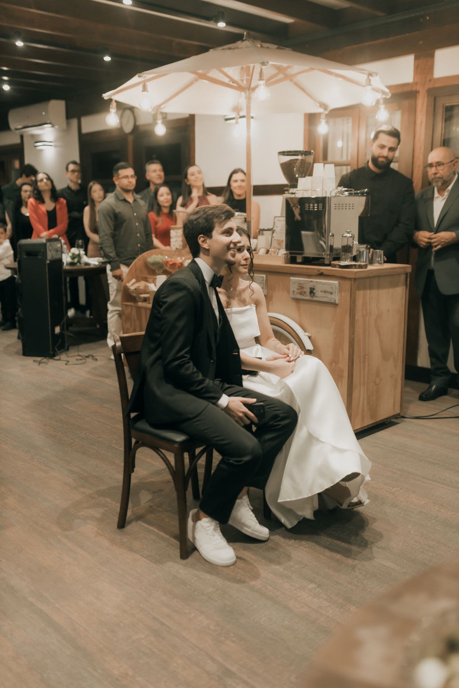 A newlywed couple seated at their reception surrounded by guests