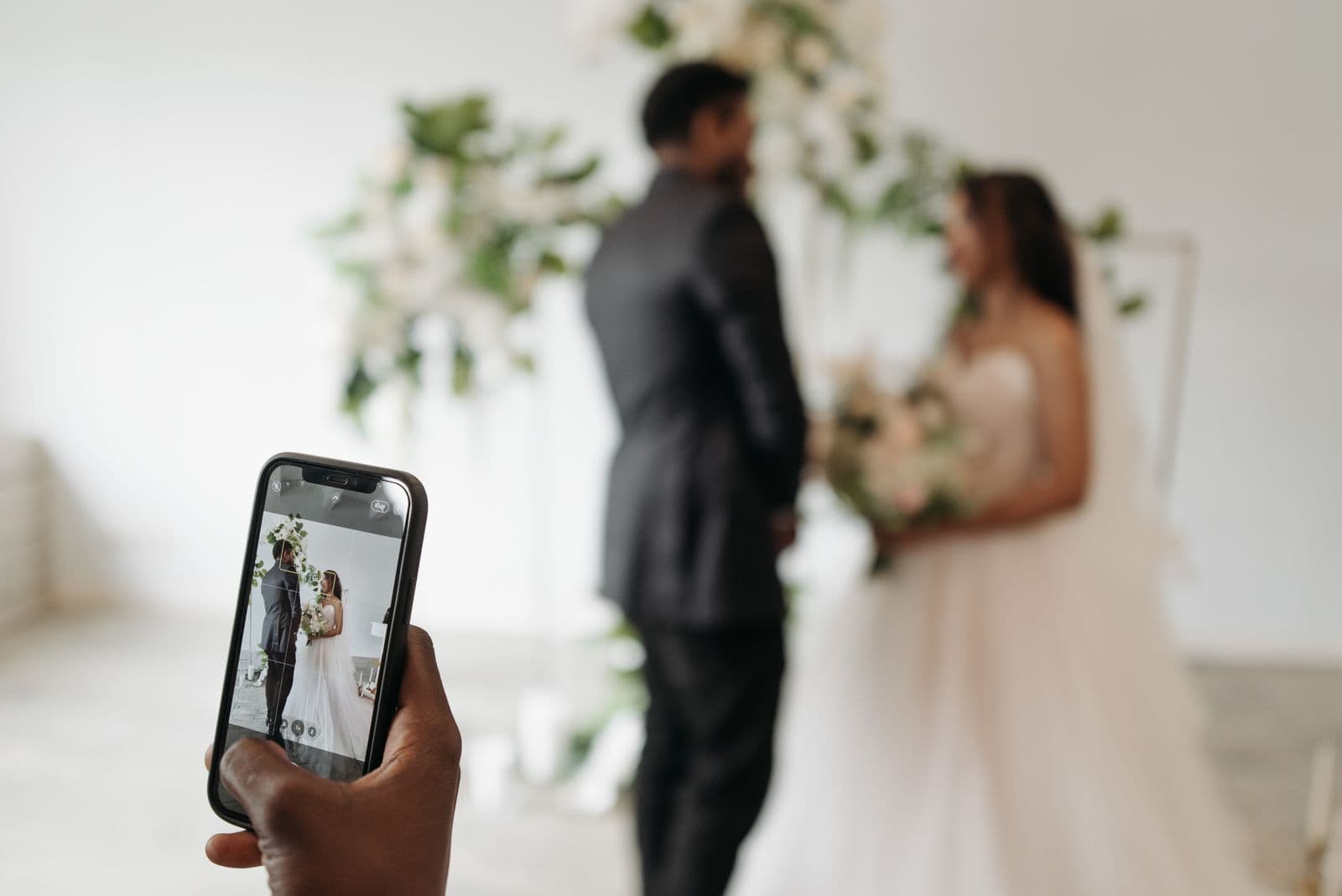 A guest photographing the bride and groom on a phone during the ceremony