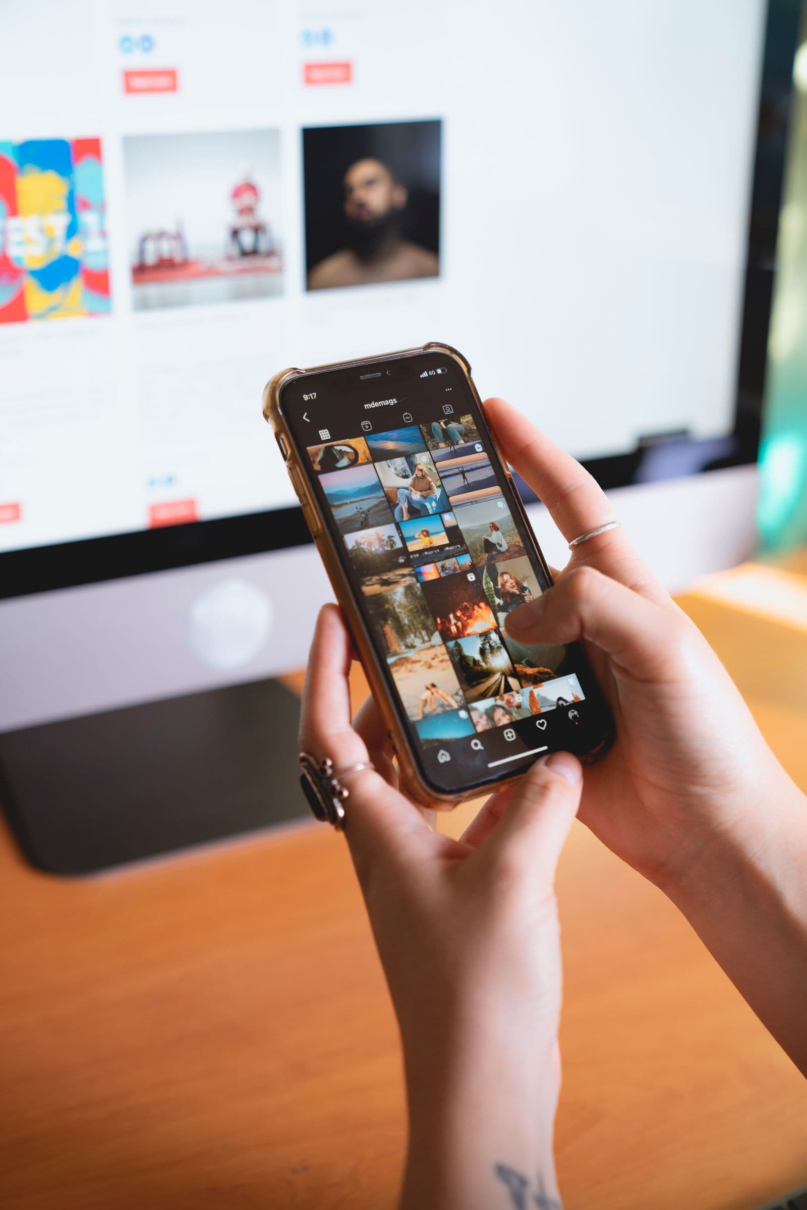 A hand holding a phone showing an Instagram profile grid of photos