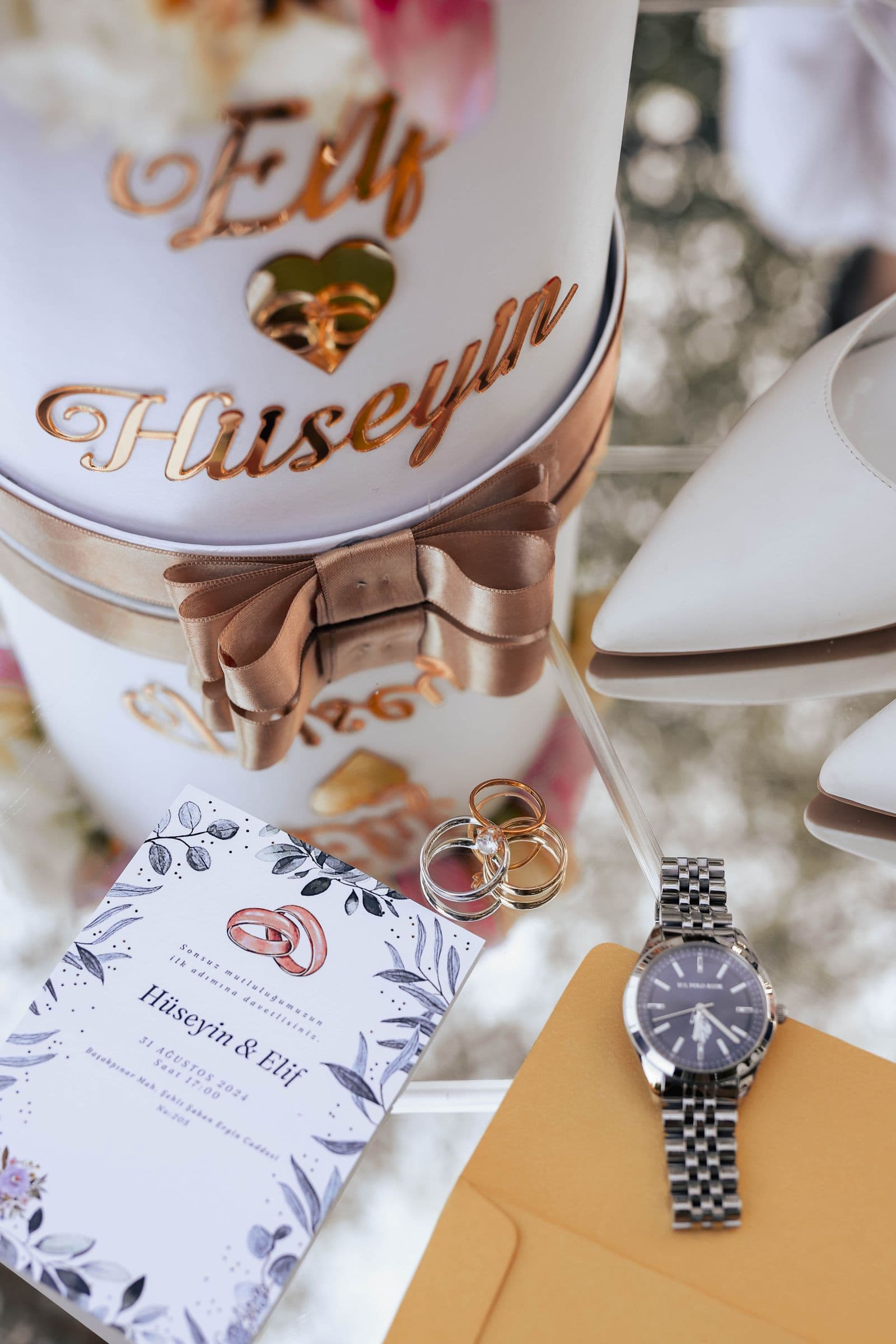 A flat lay of wedding details: invitation, rings, watch, and shoes