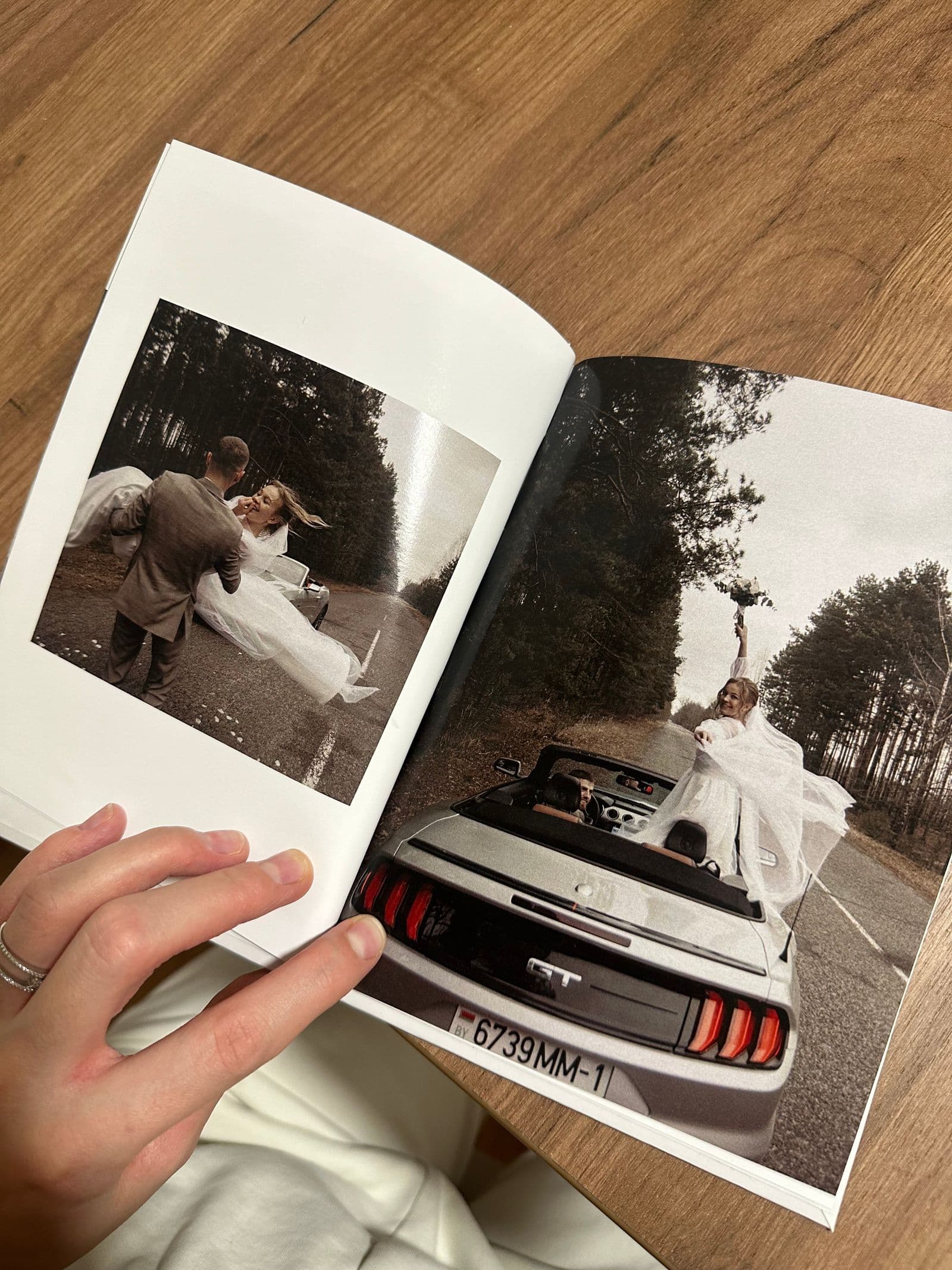 Hands holding an open printed wedding photo book showing the couple's pictures
