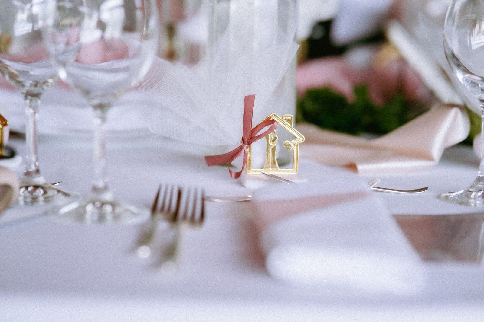A wedding place setting with glassware, cutlery, and a small decorative favor on a white table