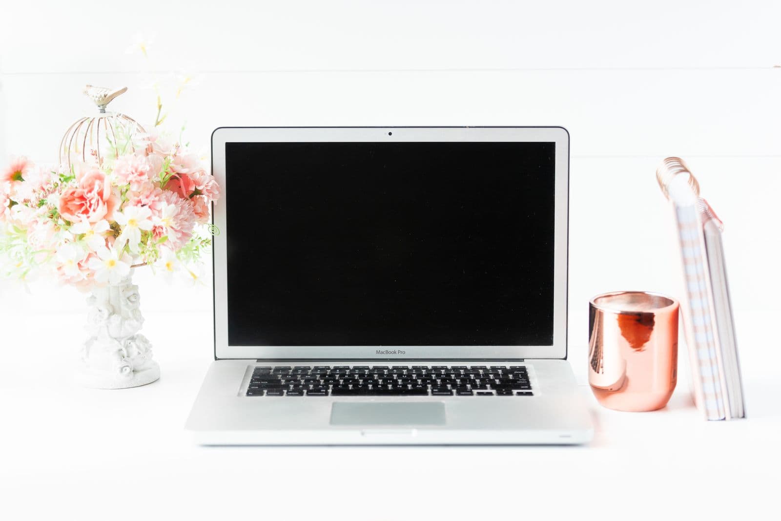 A laptop, flowers, and a notebook on a bright wedding-planning desk
