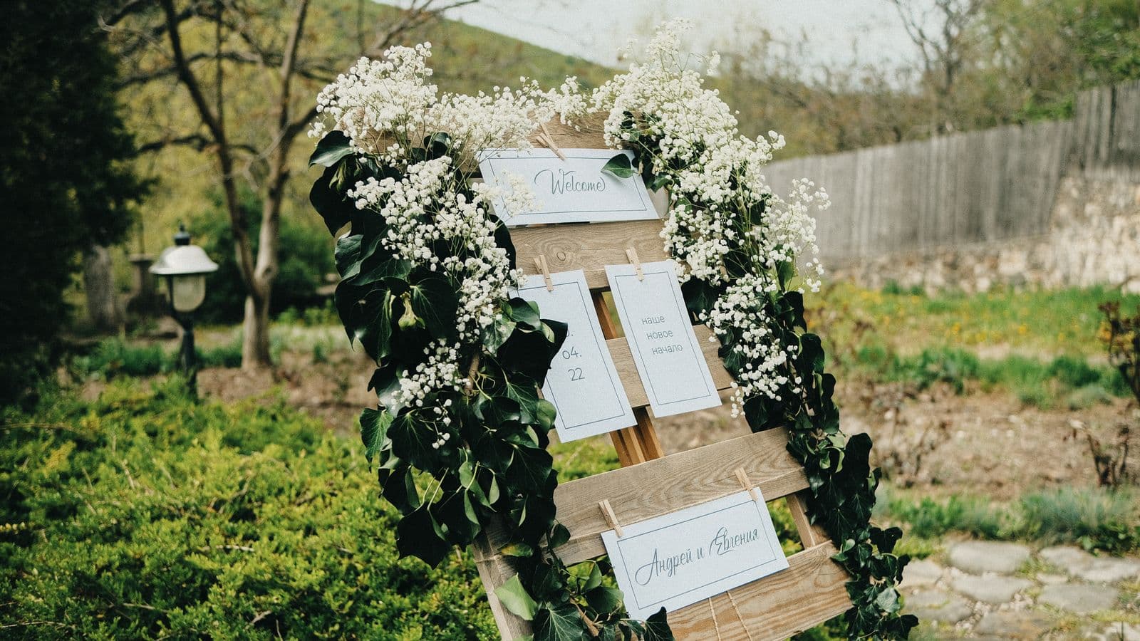 A rustic wedding welcome sign on an easel decorated with gypsophila and ivy in a garden