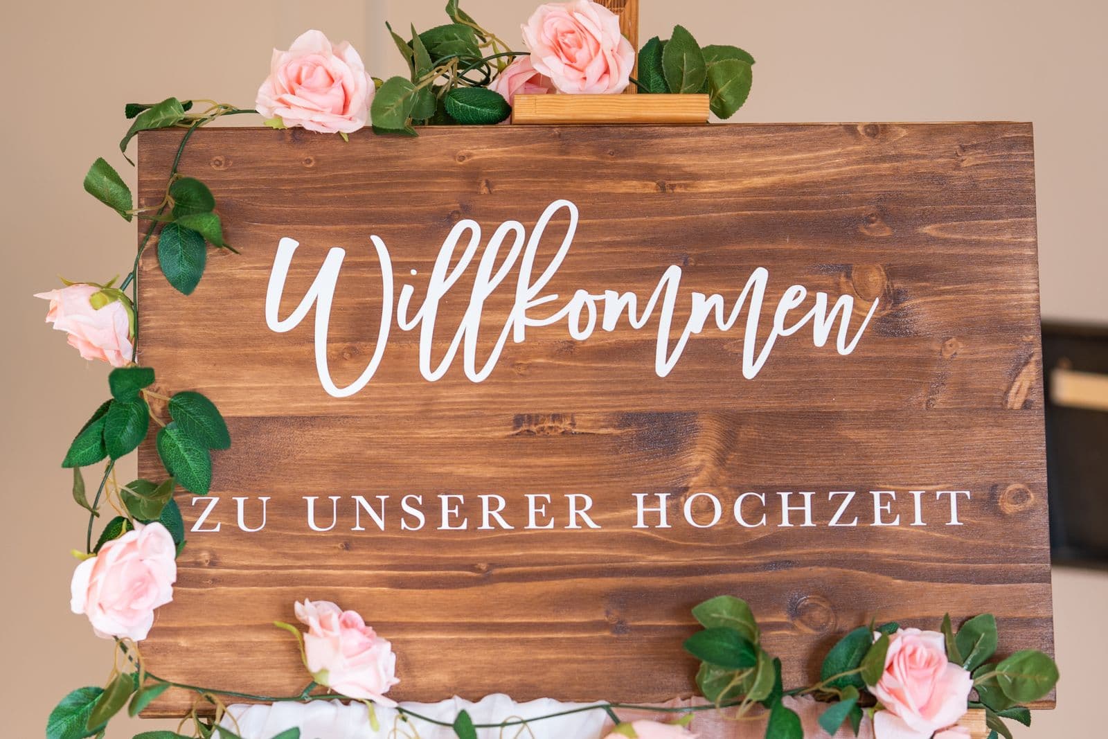 A rustic wooden welcome sign framed with pink roses at a wedding