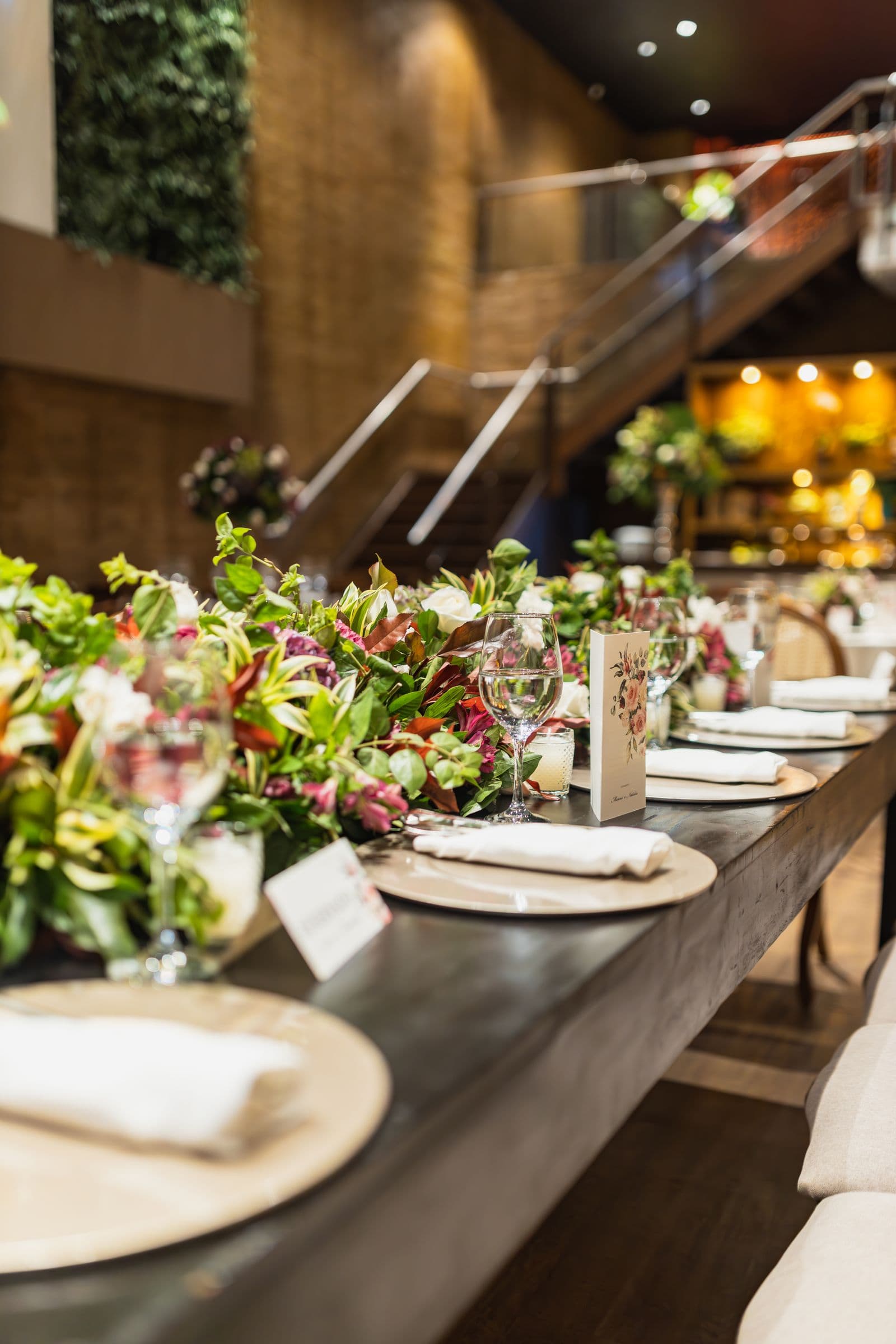 A long wedding reception table with a floral runner, place settings, and a standing menu card
