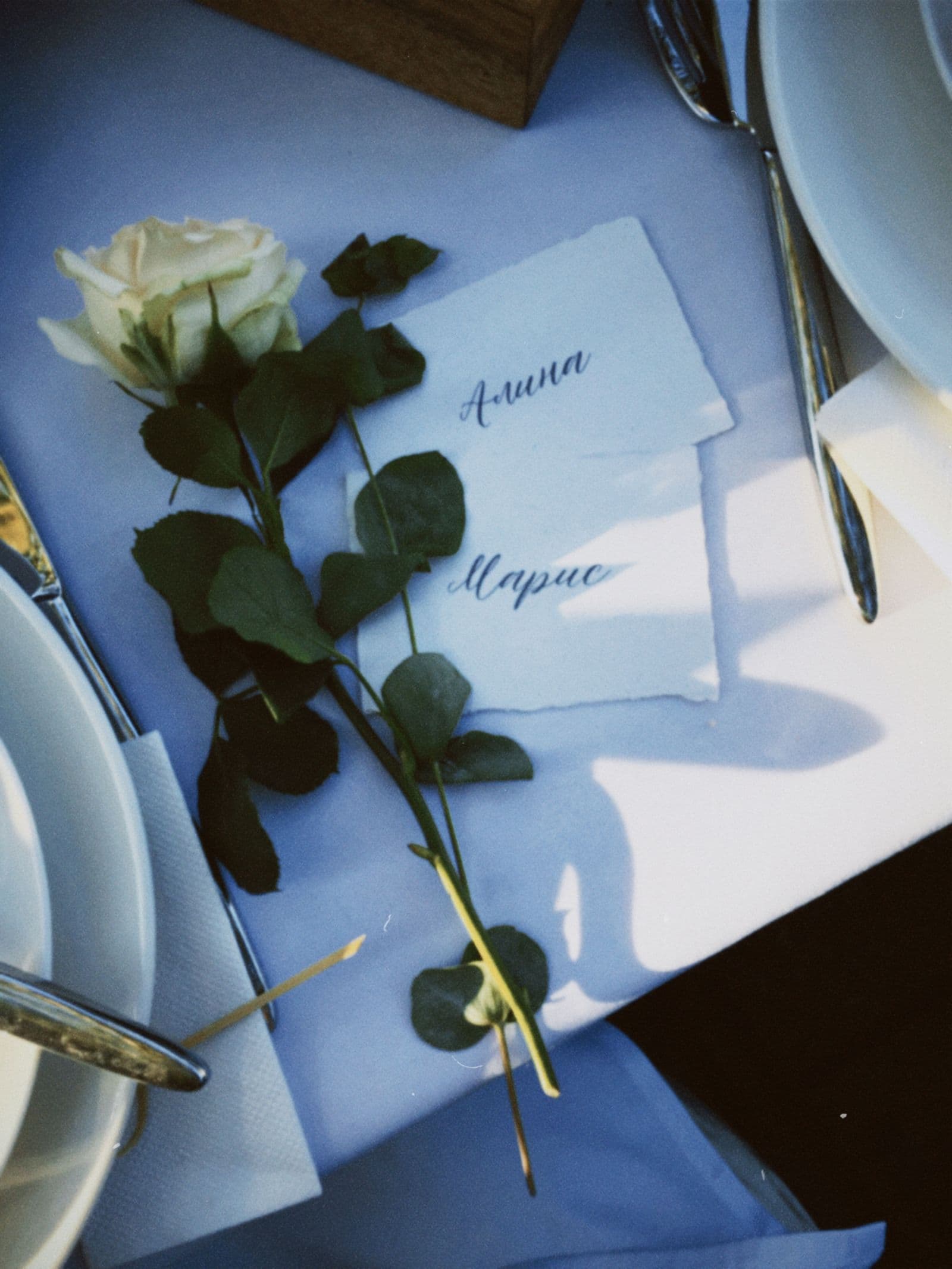 Handwritten calligraphy place cards with a white rose on a wedding place setting