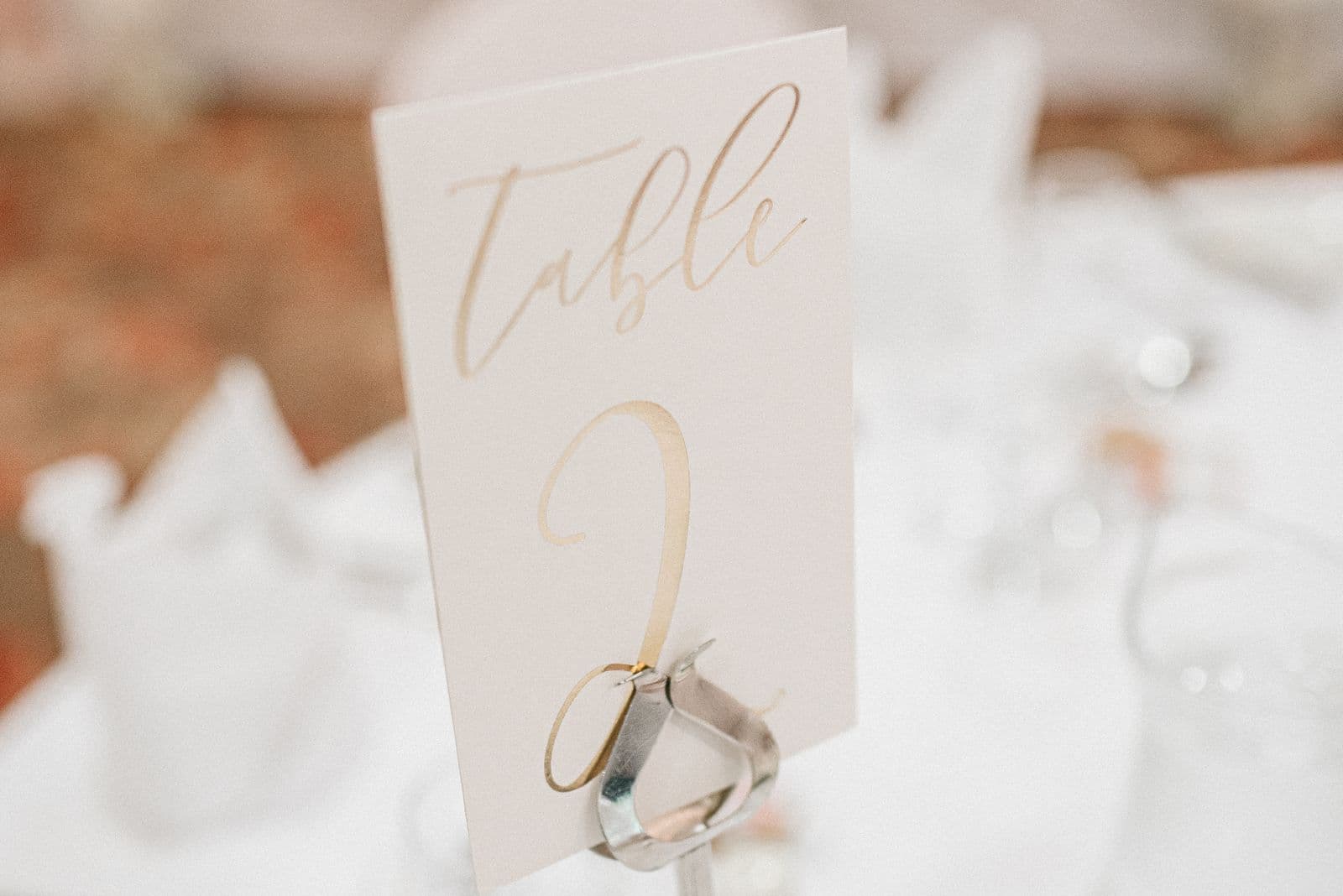 A calligraphy table number card in a holder on a set wedding reception table