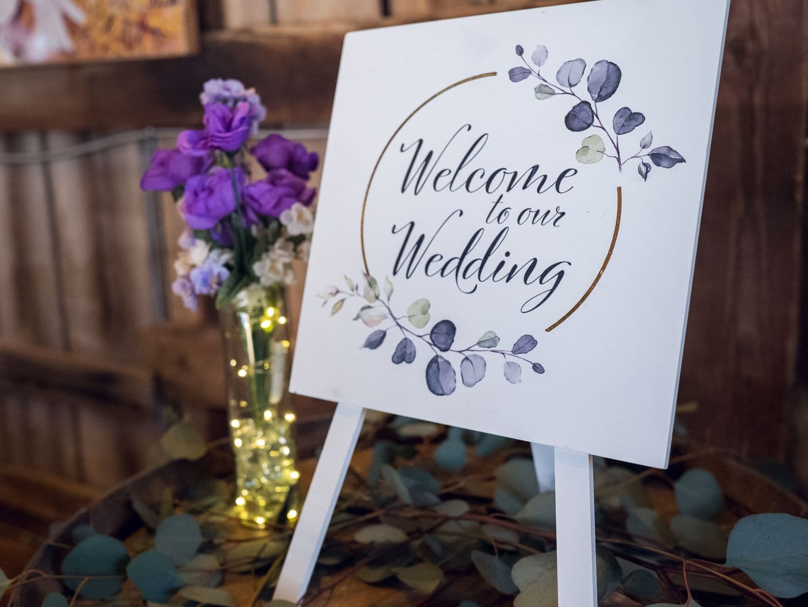 A calligraphy Welcome to our Wedding sign beside purple flowers