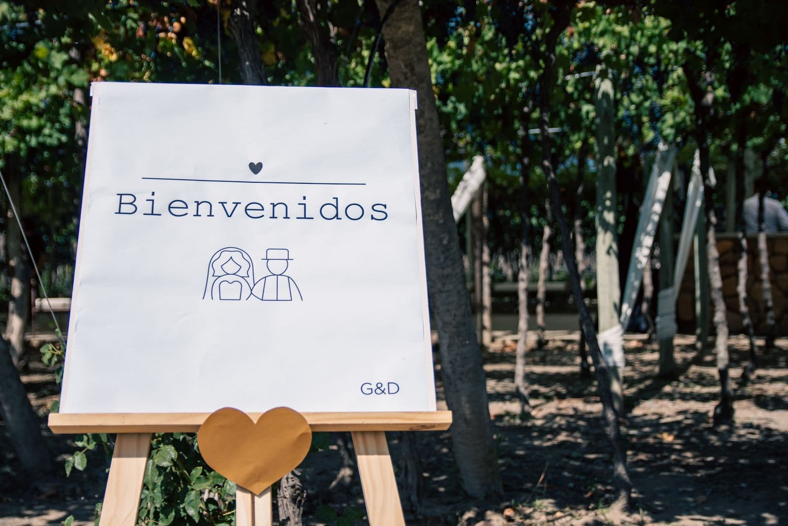 A clean printed wedding welcome sign on a wooden easel at an outdoor venue